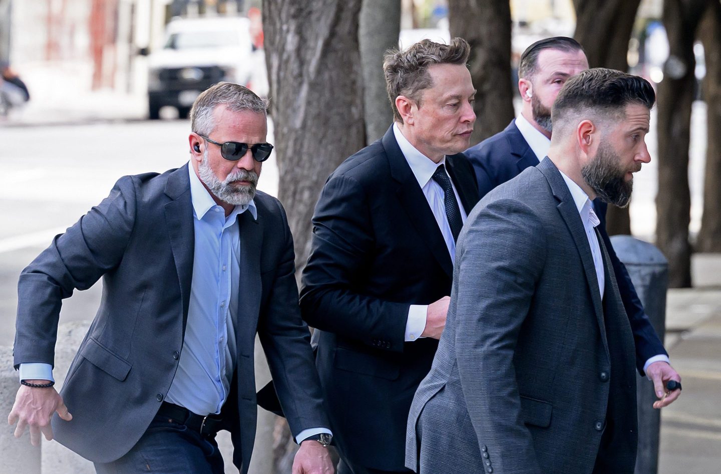 Elon Musk walks surrounded by men in suits