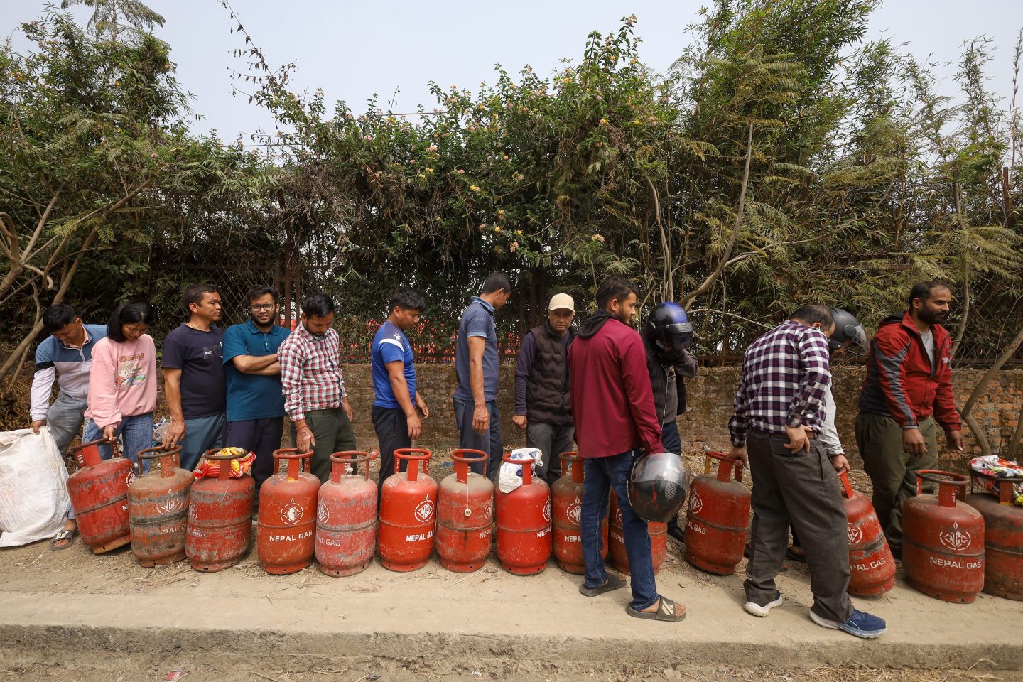 Nepali consumers wait in line carrying empty LPG cylinders as they rush to gas depots to refill them as growing tensions in West Asia halt the supply in Kathmandu, Nepal, on March 12, 2026. People wait for hours hoping to refill their gas cylinders. While some manage to purchase filled cylinders, many others return empty-handed as supplies remain limited. The disruption follows the escalating conflict involving the United States, Israel, and Iran, which heightens tensions across the Gulf region. Shipping through the Strait of Hormuz, a key maritime route bordering Iran, the United Arab Emirates, and Oman, is also affected by the conflict, disrupting the transport of gas and petroleum products. The impact is now felt in markets around the world.
