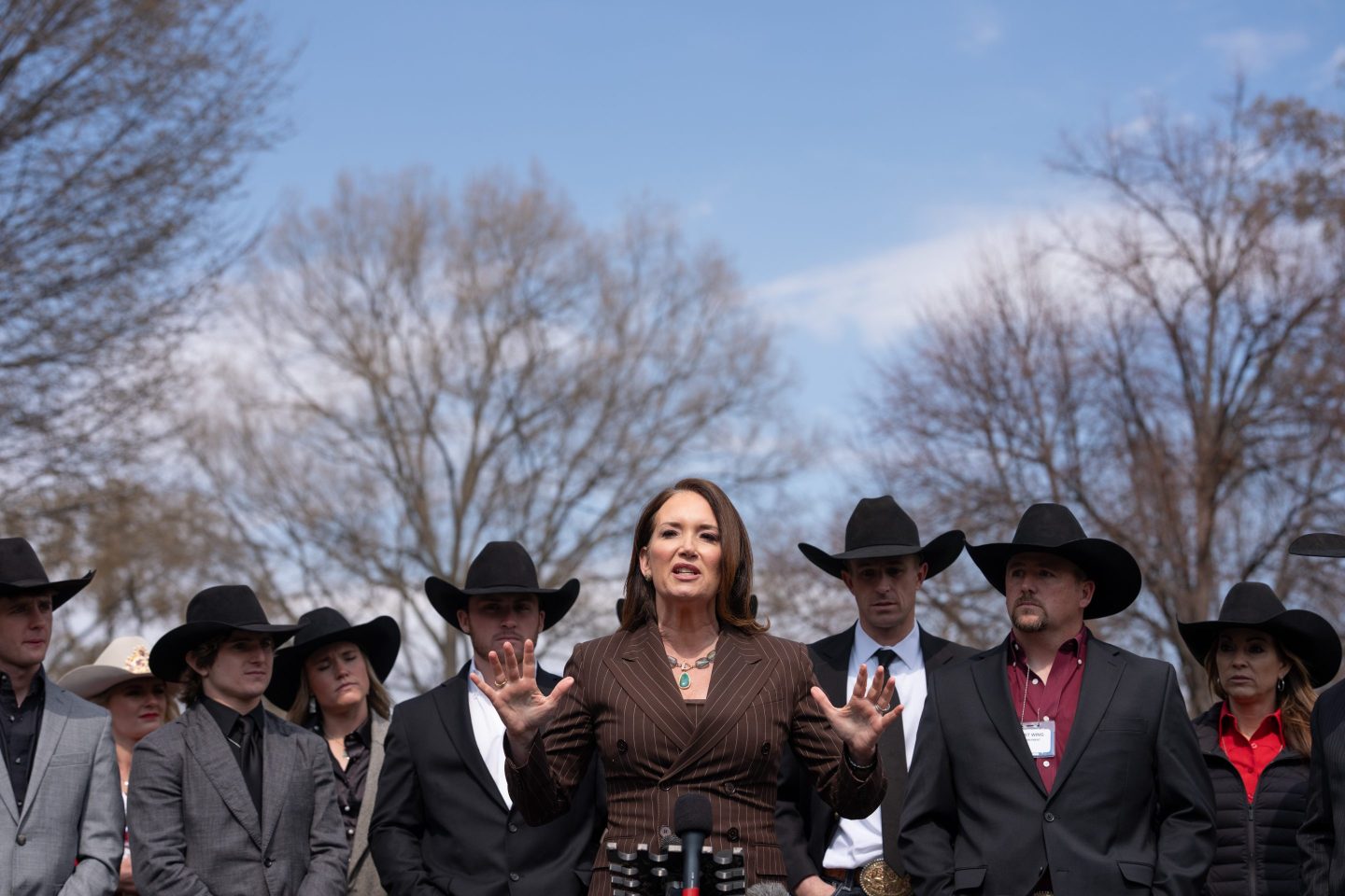 Brooke Rollins stands in front of a line of men wearing black cowboy hats.