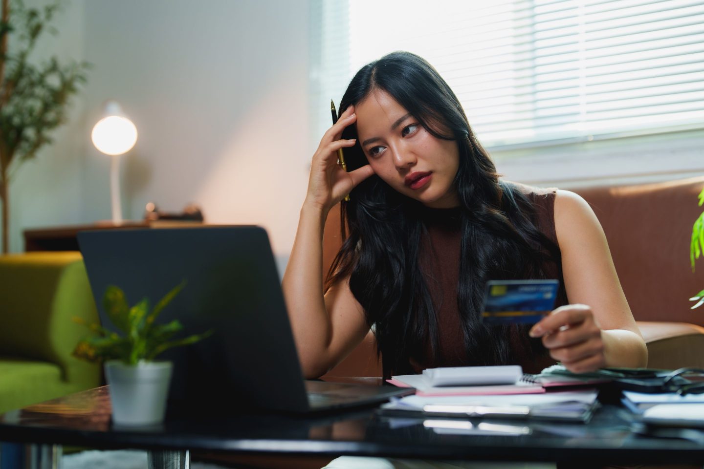 Young woman looks at her computer looking stressed and holding a credit card