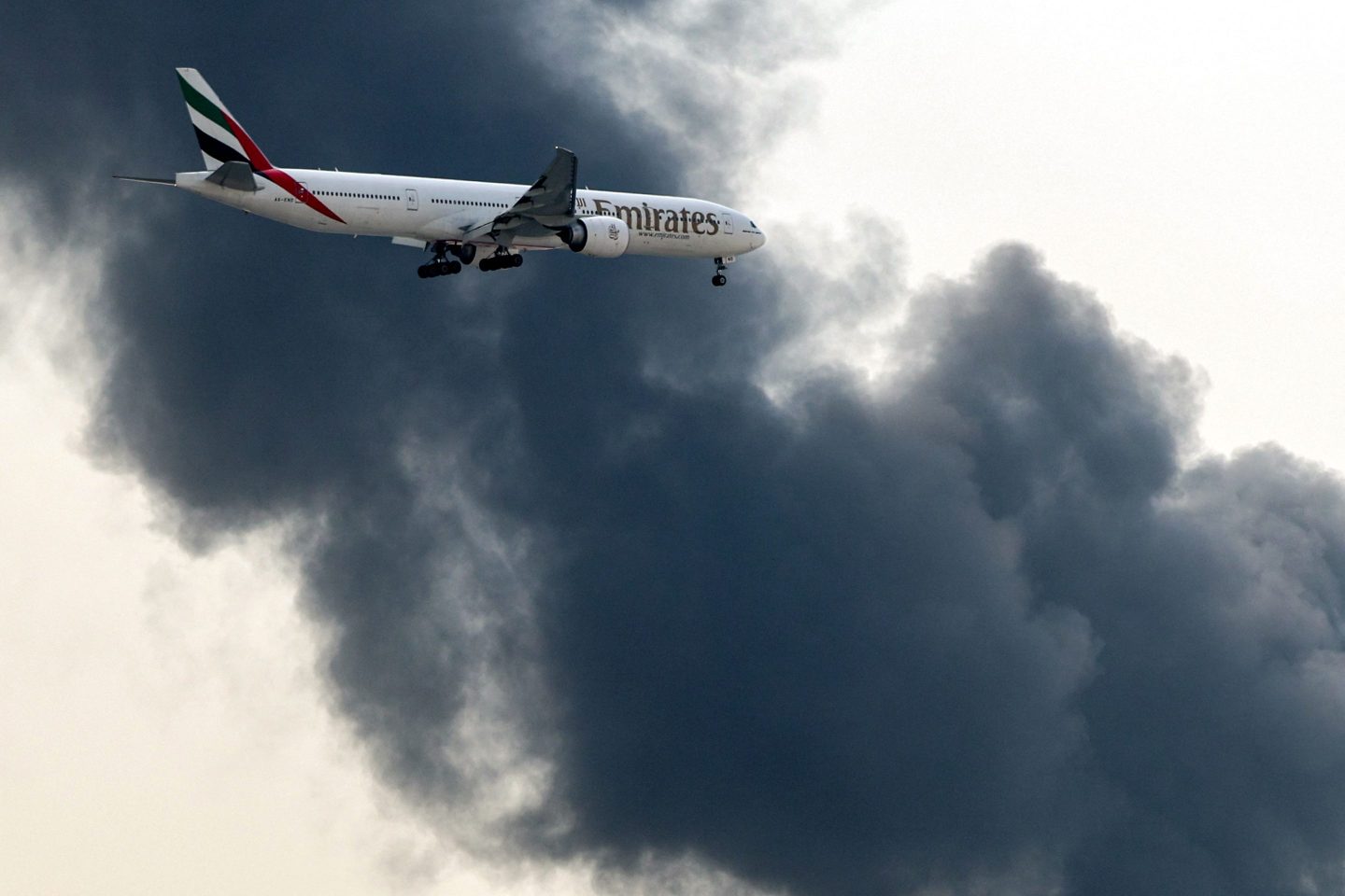 TOPSHOT - CORRECTION / An Emirates Boeing 777 aircraft prepares for landing as a smoke plume rises from an ongoing fire near Dubai International Airport in Dubai on March 16, 2026. Flights were gradually resuming at Dubai airport on March 16, previously the world's busiest for international flights, the airport operator said, after a "drone-related incident" sparked a fuel tank fire nearby, as Iran kept up its Gulf attacks. (Photo by AFP via Getty Images) / "The erroneous mention[s] appearing in the metadata of this photo by - has been modified in AFP systems in the following manner: [Boeing 777] instead of [Airbus A350]. Please immediately remove the erroneous mention[s] from all your online services and delete it (them) from your servers. If you have been authorized by AFP to distribute it (them) to third parties, please ensure that the same actions are carried out by them. Failure to promptly comply with these instructions will entail liability on your part for any continued or post notification usage. Therefore we thank you very much for all your attention and prompt action. We are sorry for the inconvenience this notification may cause and remain at your disposal for any further information you may require."
