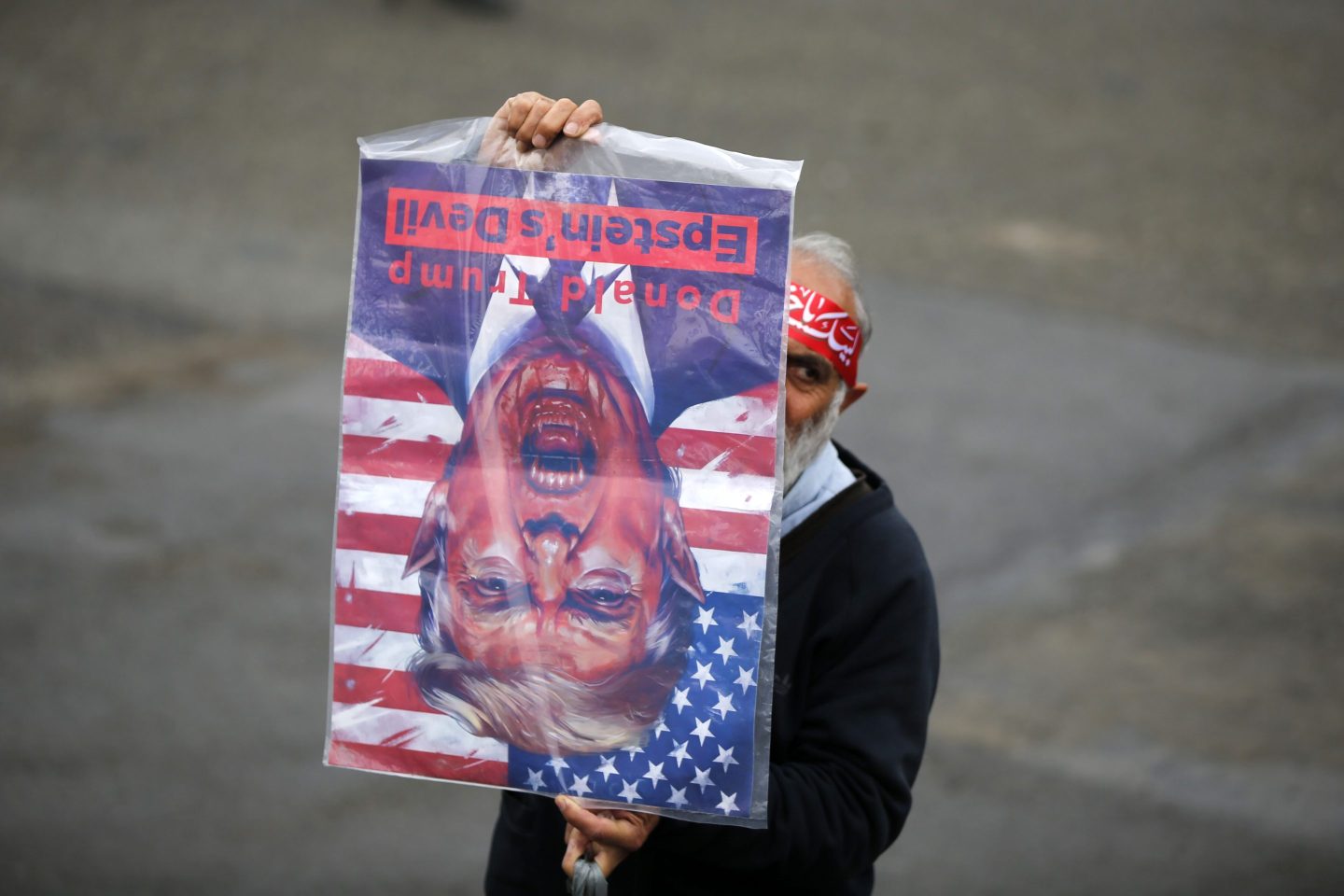 A man holds a poster upside down that depicts Donald Trump as the devil.