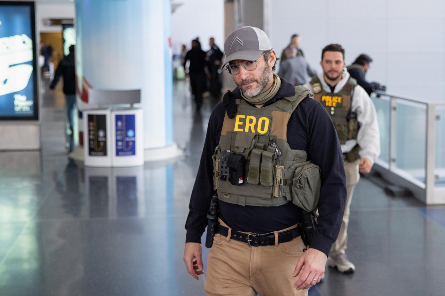 A man in a green ERO vest walks through an airport terminal.