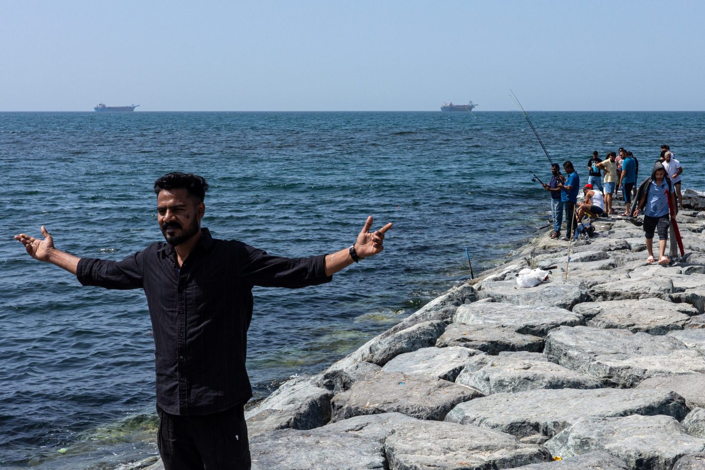 People on a breakwater backdropped by commercial vessels anchored in the Gulf, near the Strait of Hormuz, on March 22, 2026 in Ajman, United Arab Emirates.