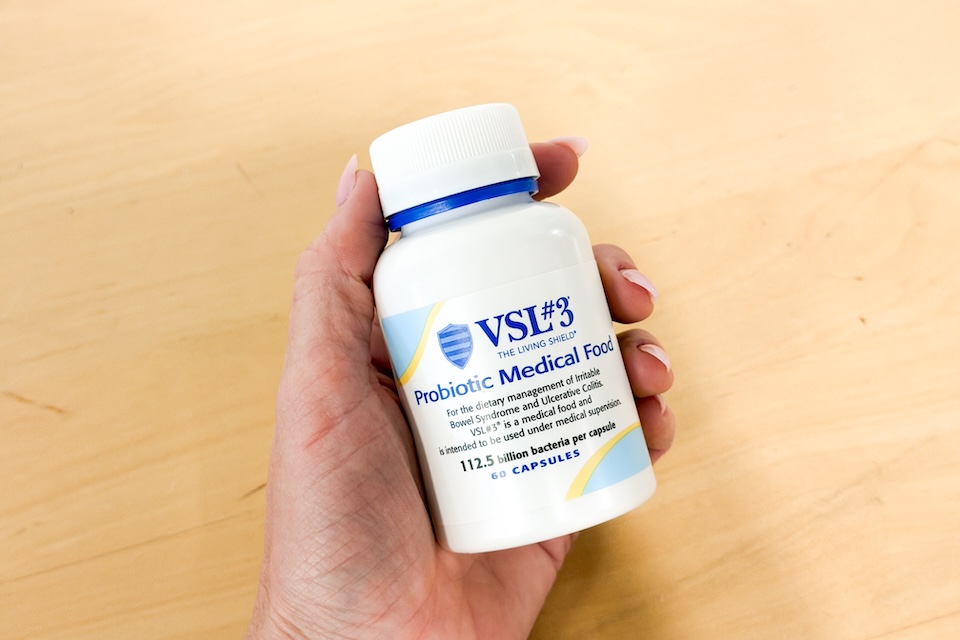 A close-up shot of a woman's hand holding a bottle of VSL#3 Probiotics.