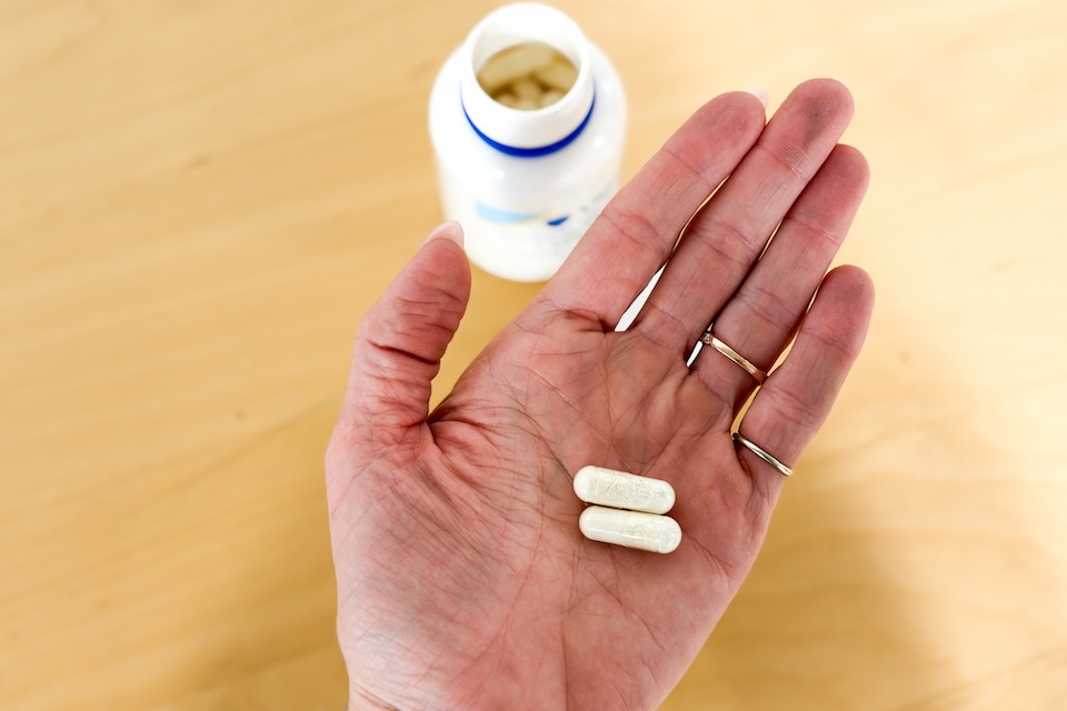 A close-up shot of a woman's open palm holding two capsules of VSL#3 Probiotics.