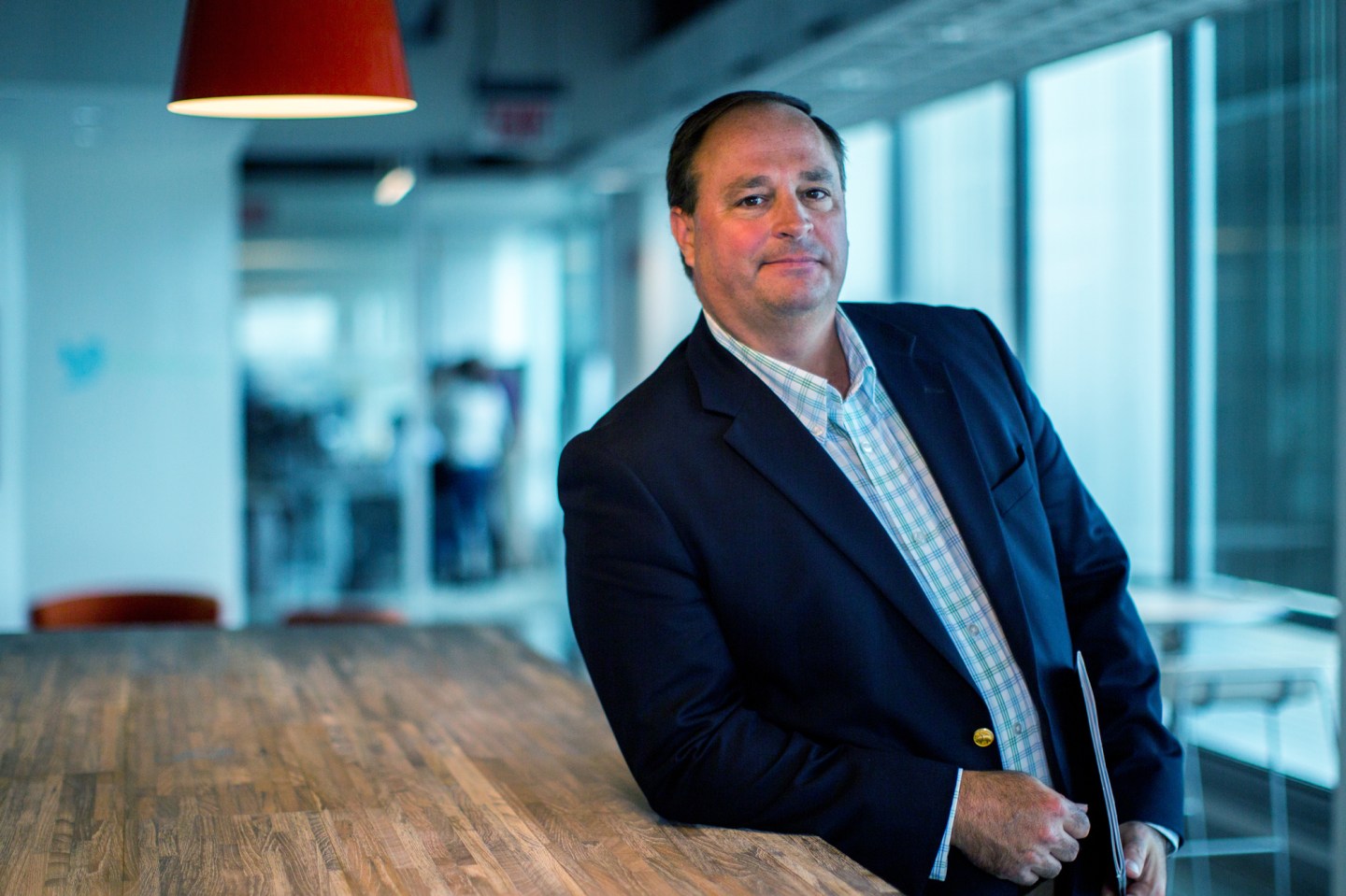 A man in a suit stands leaning against a table.