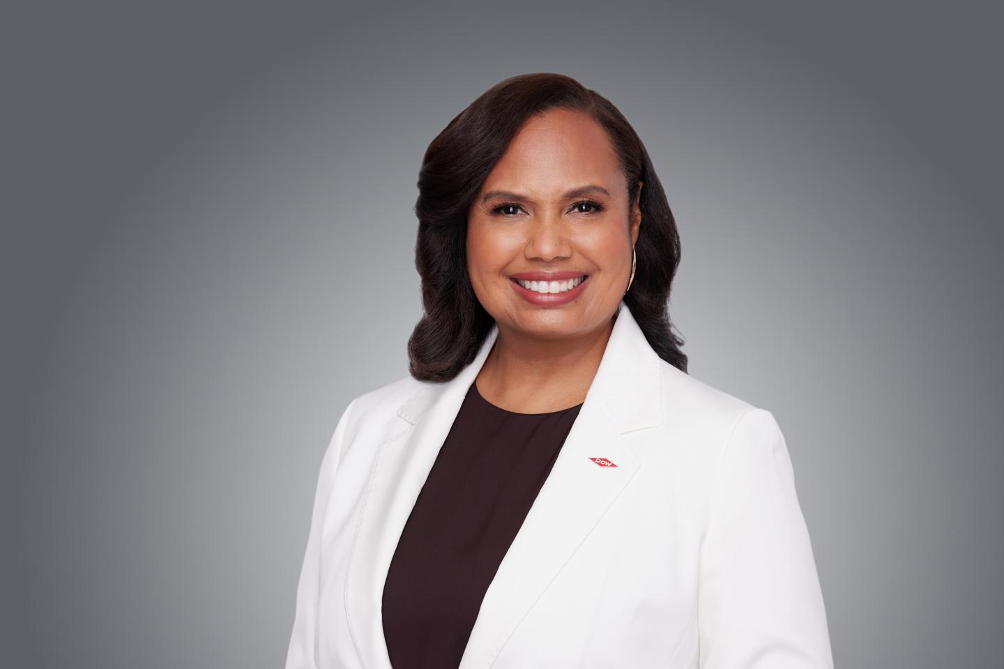 Dow COO Karen Carter wearing a white lab coat and sitting while smiling