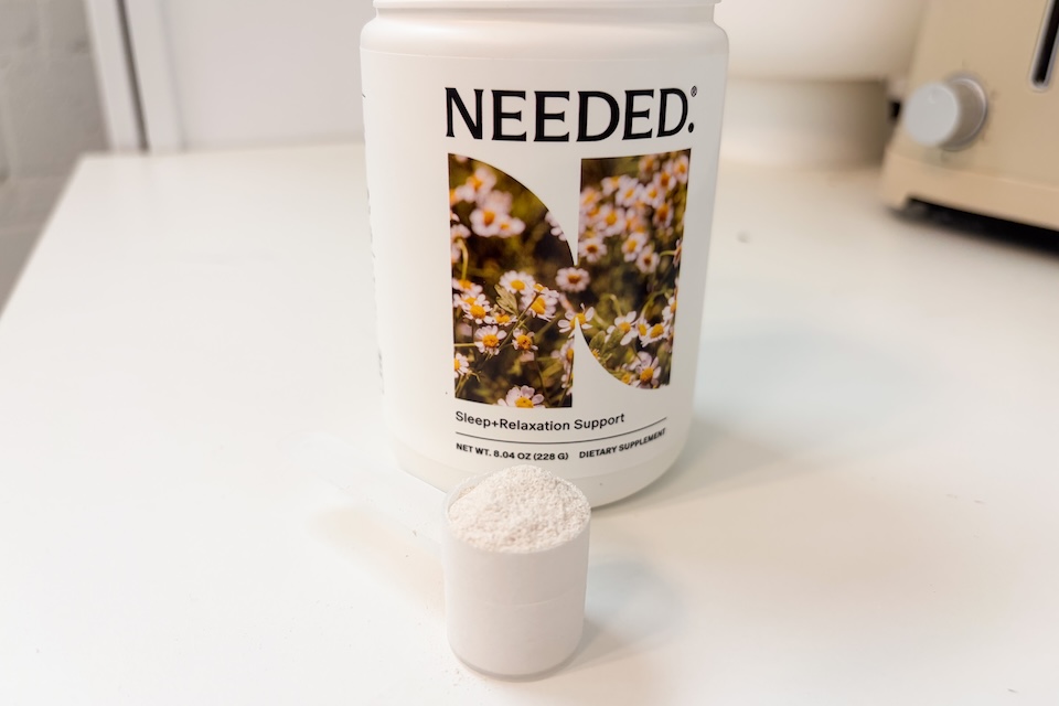 A scoop of Needed Sleep and Relaxation Support sitting on a countertop in front of the bottle.