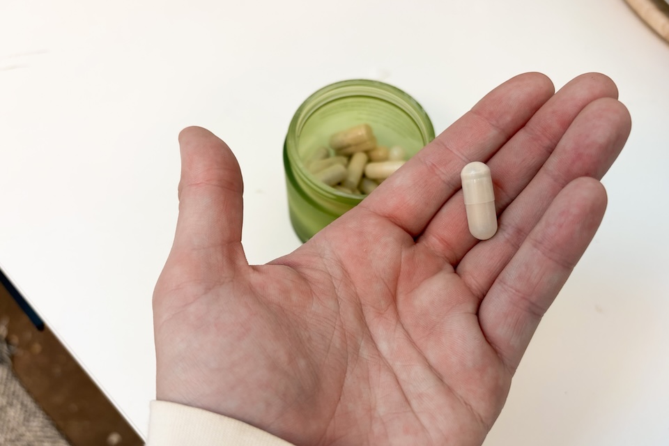 An open palm holding a Seed DM-02 capsule. On a countertop below, you can see an open bottle containing more of the capsules.