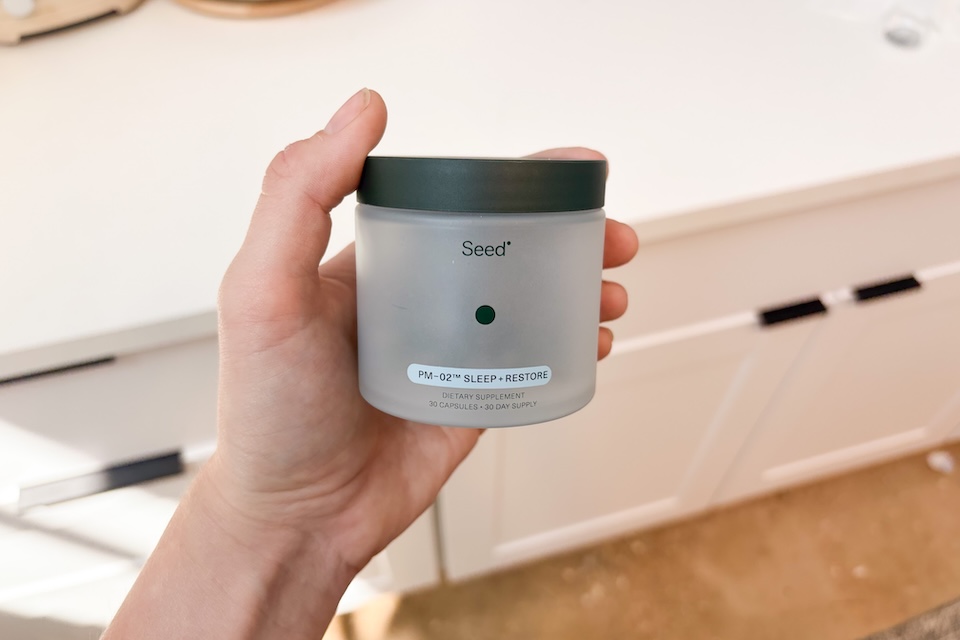 A hand holding a jar of Seed PM-02 supplements