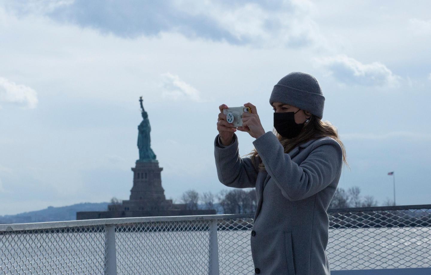 A woman taking a picture of the Statue of Liberty.