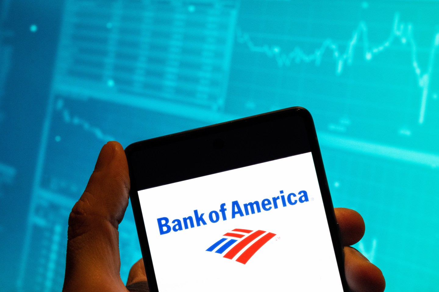 In this photo illustration, the American multinational investment bank and financial services company, The Bank of America (NYSE: BAC) logo is seen displayed on a smartphone with an economic stock exchange index graph in the background.