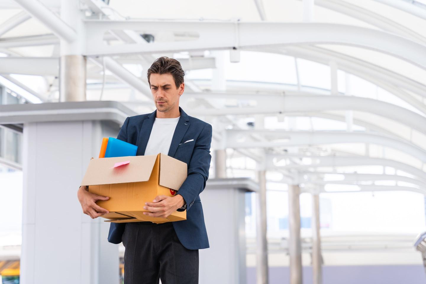 Businessman being fired by company downsizing carrying a box of personal items