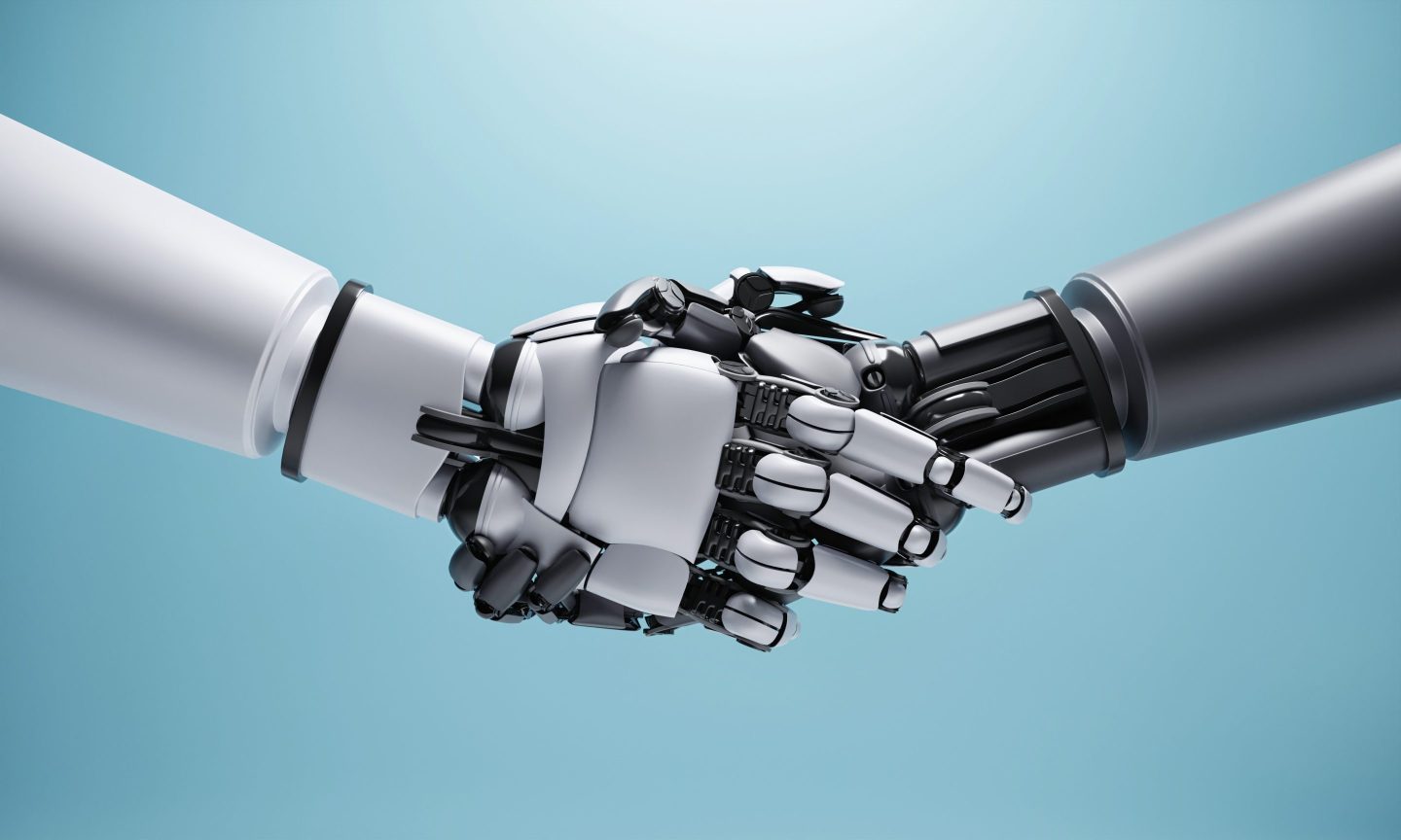 One humanoid robot handing shaking hands with another humanoid robotic hand. One robot on the left is lighter metal colored than the one on the right.