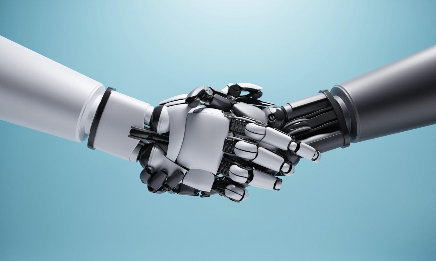 One humanoid robot handing shaking hands with another humanoid robotic hand. One robot on the left is lighter metal colored than the one on the right.