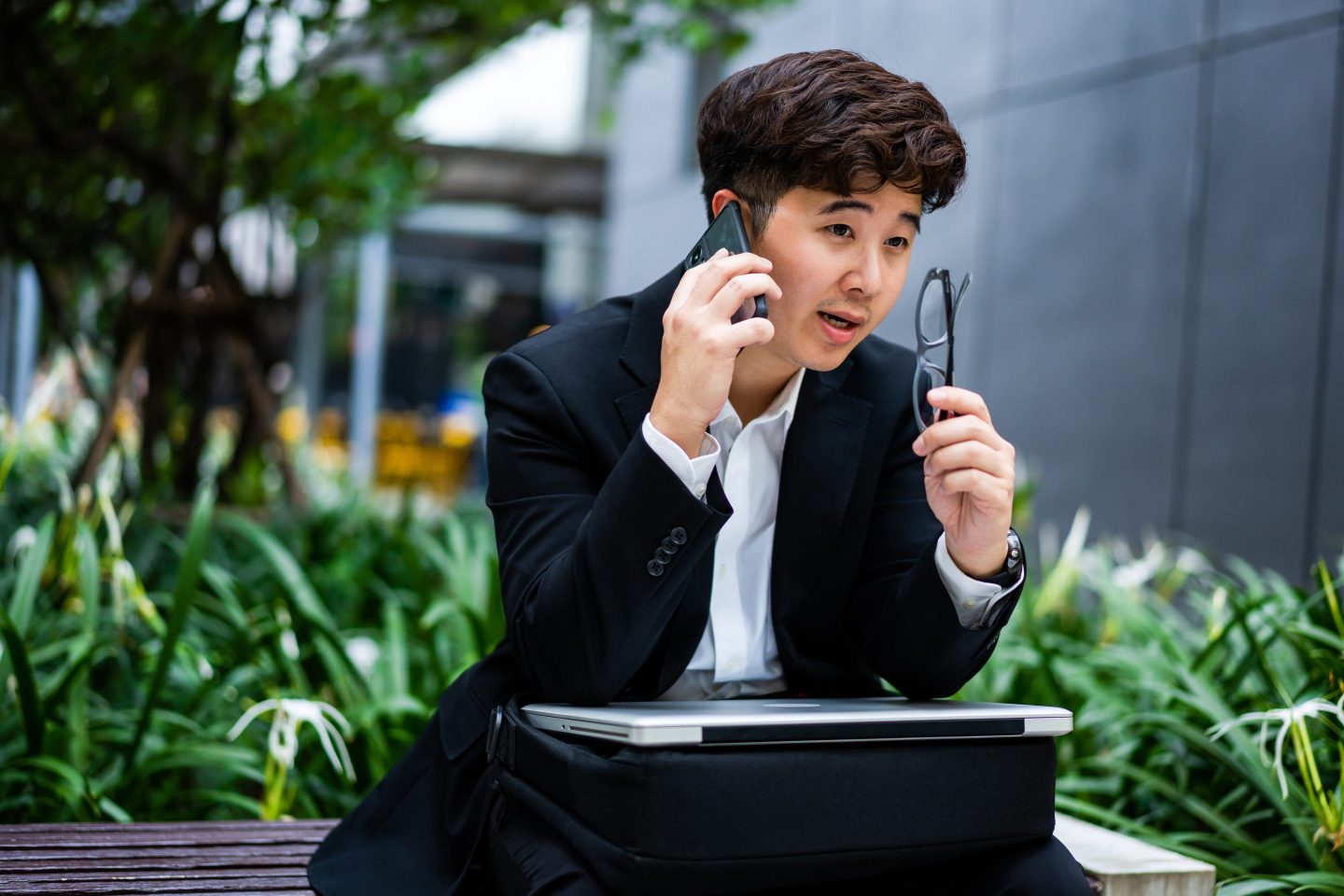 Asian man talking on the phone with his laptop in his lap