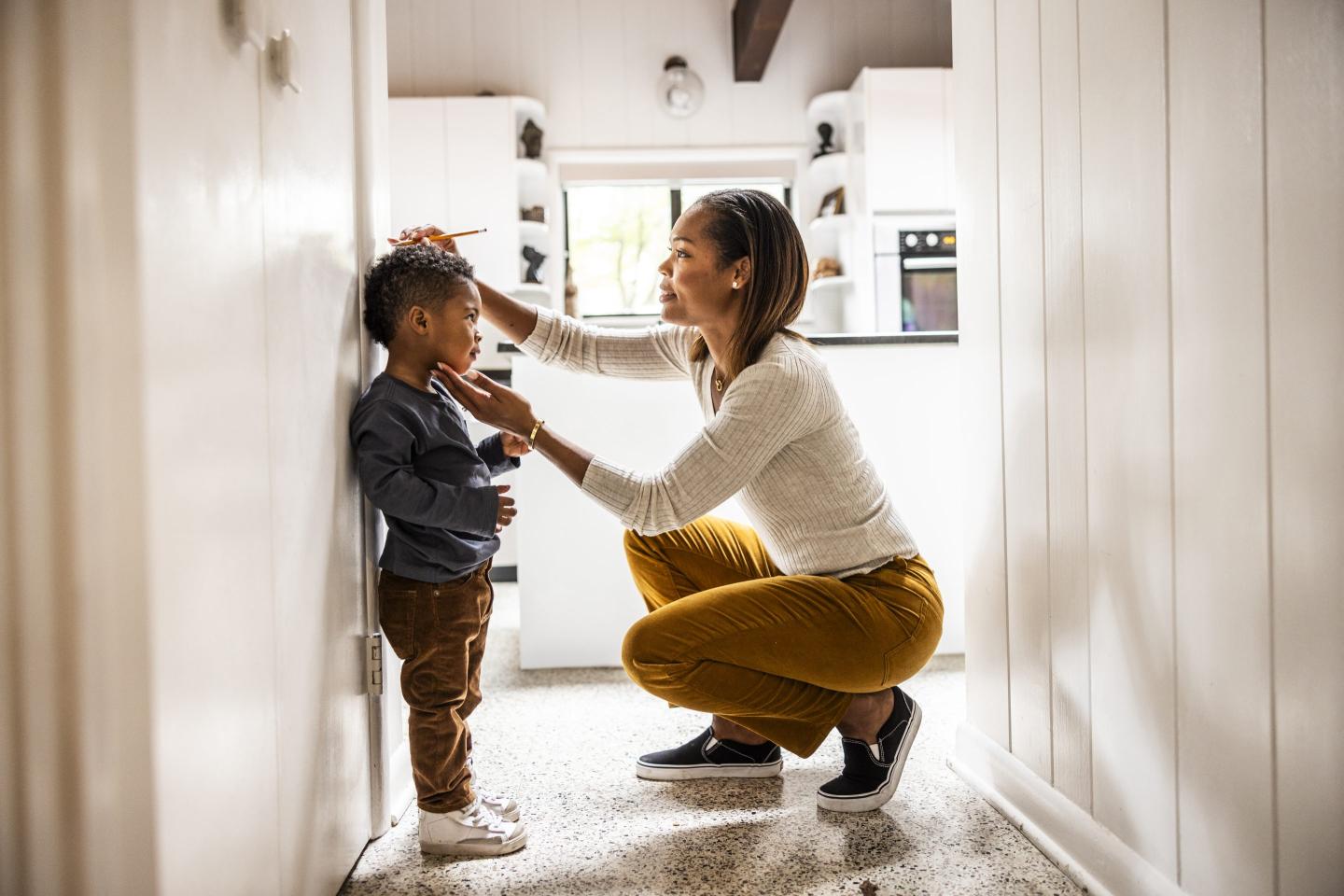 A woman measures a little boy's height against the kitchen wall