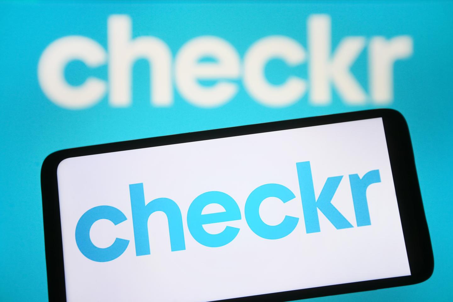 In this photo illustration, Checkr logo is seen on a smartphone and on a pc screen.