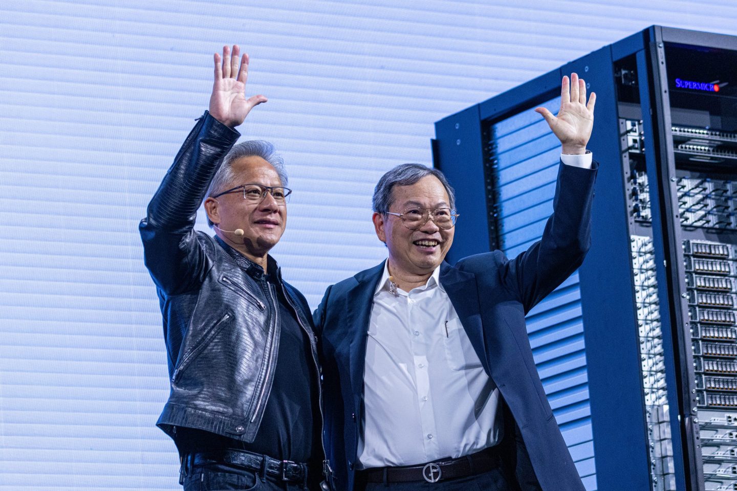 two men waving in front of server racks
