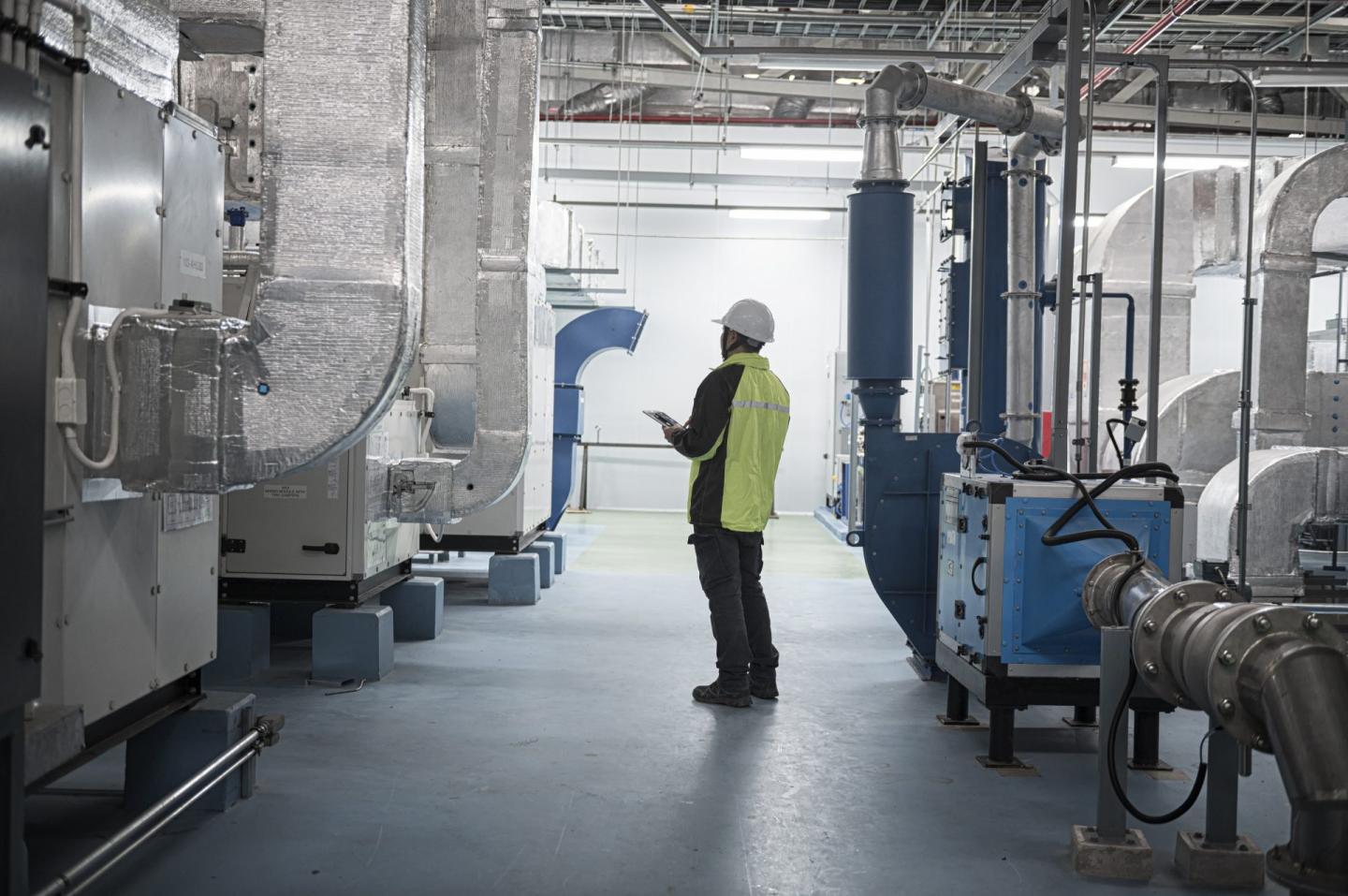 A technician in safety gear performs a routine inspection inside a modern industrial facility