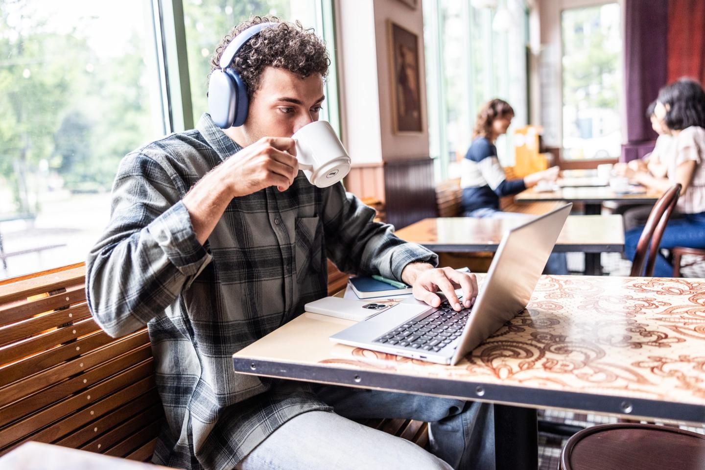 Young man working on a laptop drinks coffee in a restaurant