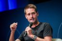 Evan Spiegel wears a black t-shirt and speaks into a microphone while on stage.