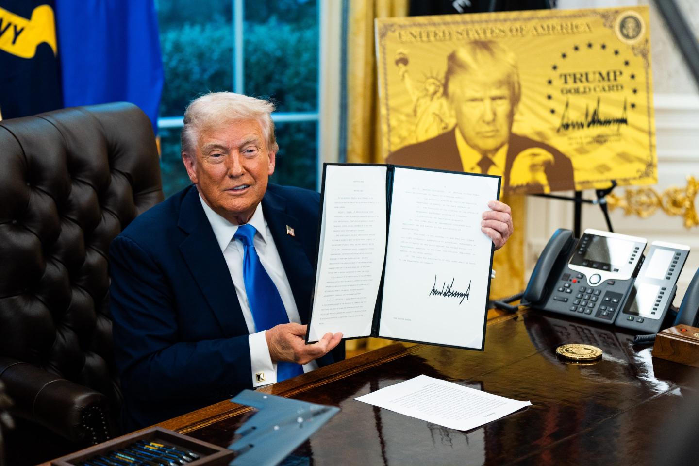Trump holds the bill up.