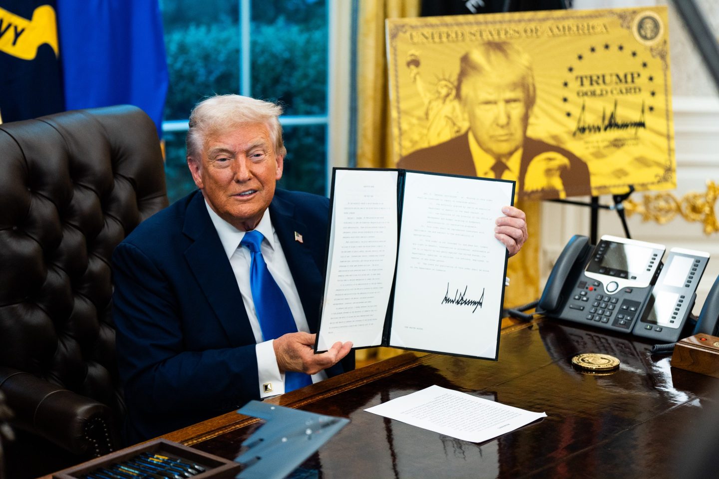 Trump holds the bill up.