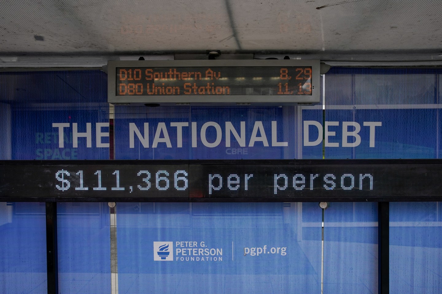 A view of a bus shelter at Pennsylvania Avenue and 22nd Street NW where an electronic billboard and a poster display the current U.S. National debt per person and as a nation at 38 Trillion dollars on October 28, 2025 in Washington, DC.