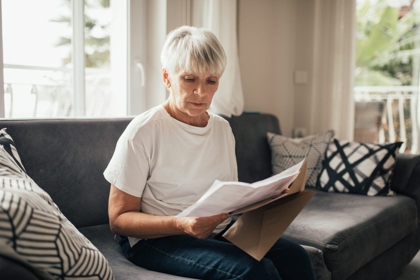Elderly woman received mail with invoices, utility bills, credit payments or bank statement. She serious and concentrated. Paperwork at home. Household routine and chores.