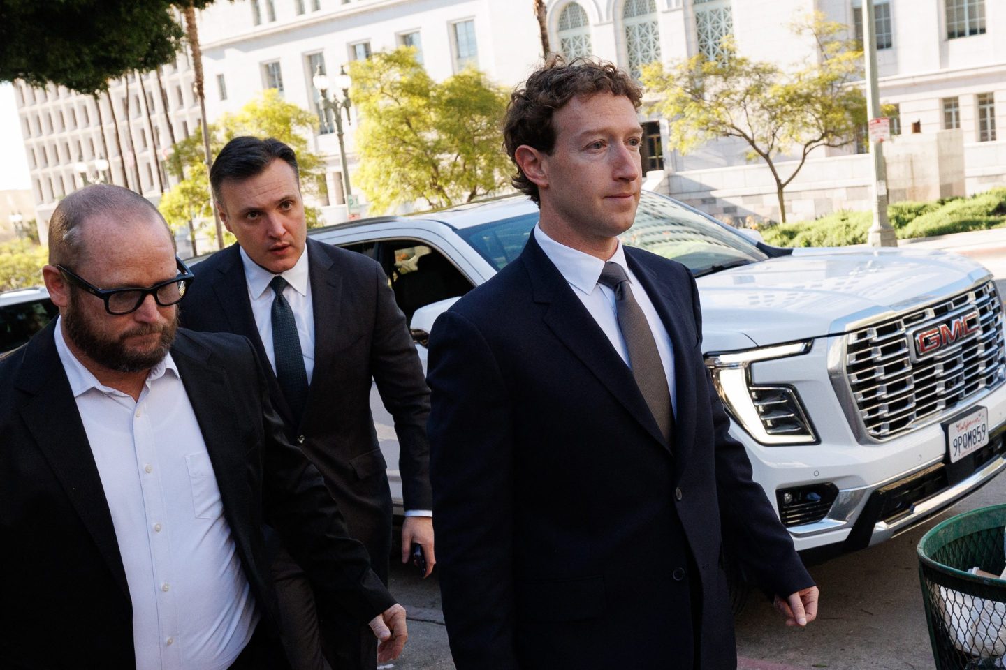 Zuckerberg, dressed a black suit, walks away from a white car.