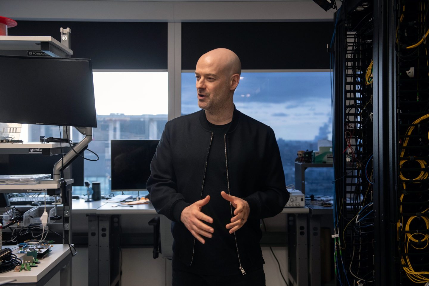 Christian Weedbrook standing in an office wearing a black jacket.