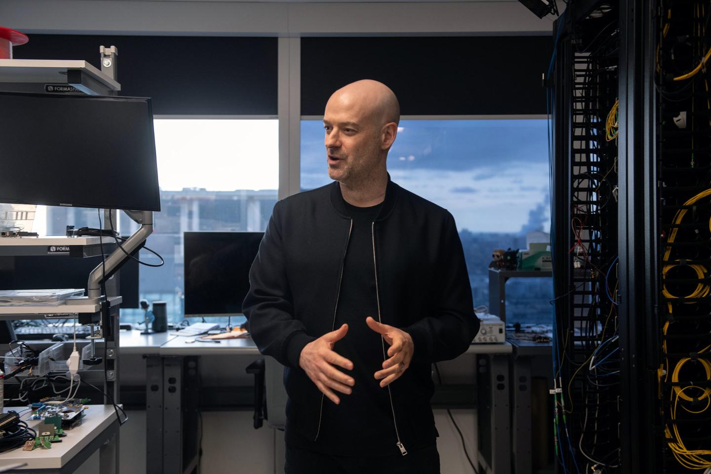 Christian Weedbrook standing in an office wearing a black jacket.