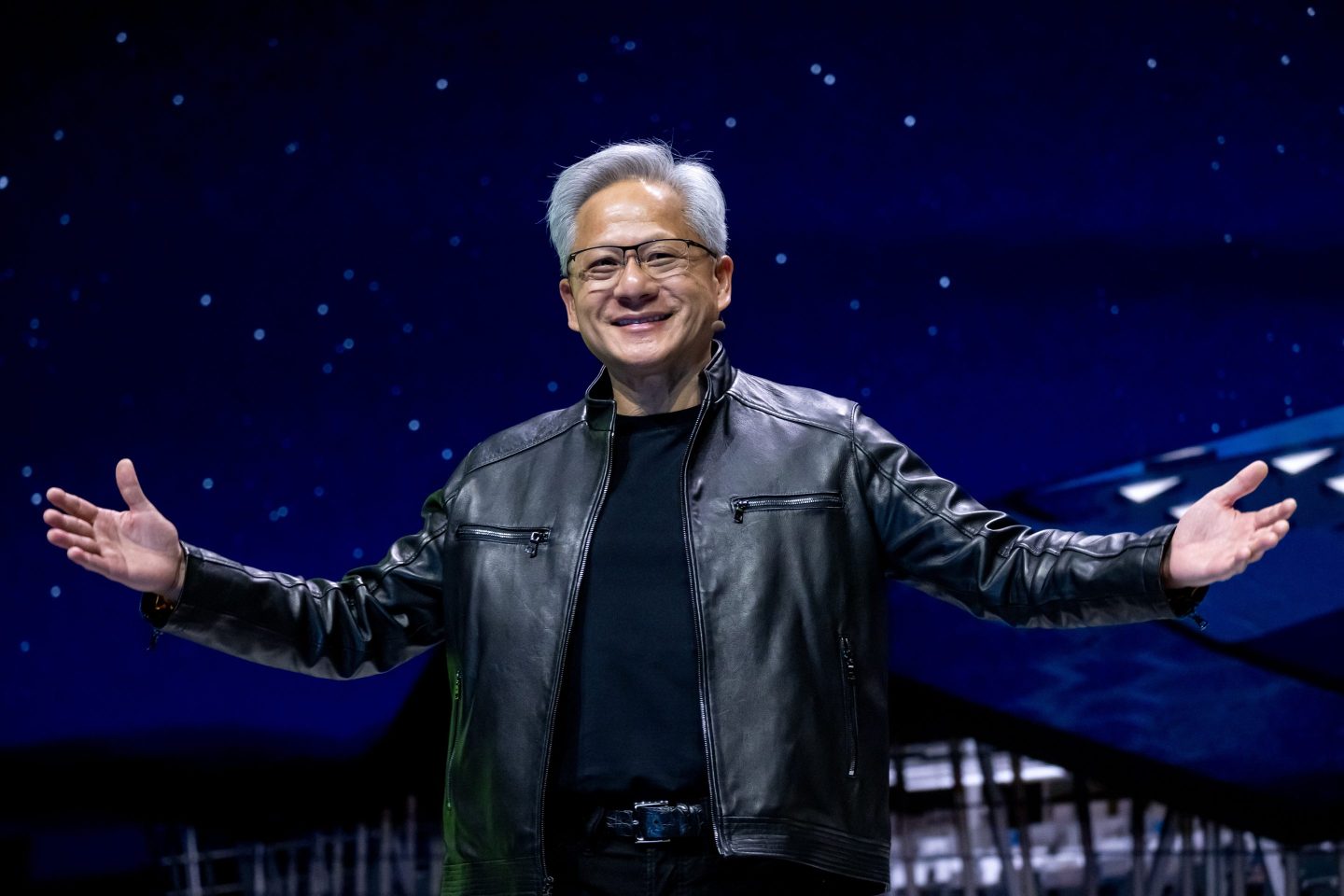Jensen Huang stands smiling with his arms outstretched.