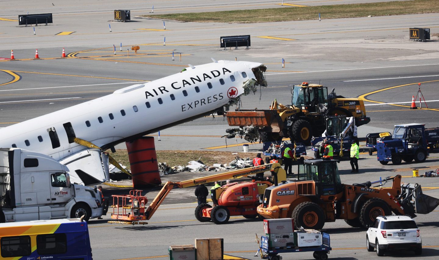 A broken grounded plane sits on the tarmac surrounded by machinery