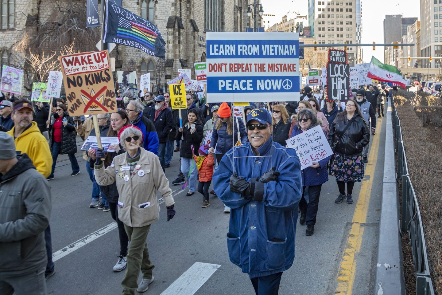 A older man walks with a sign that says "Learn from Vietnan. Don't repeat the mistake. Peace now."