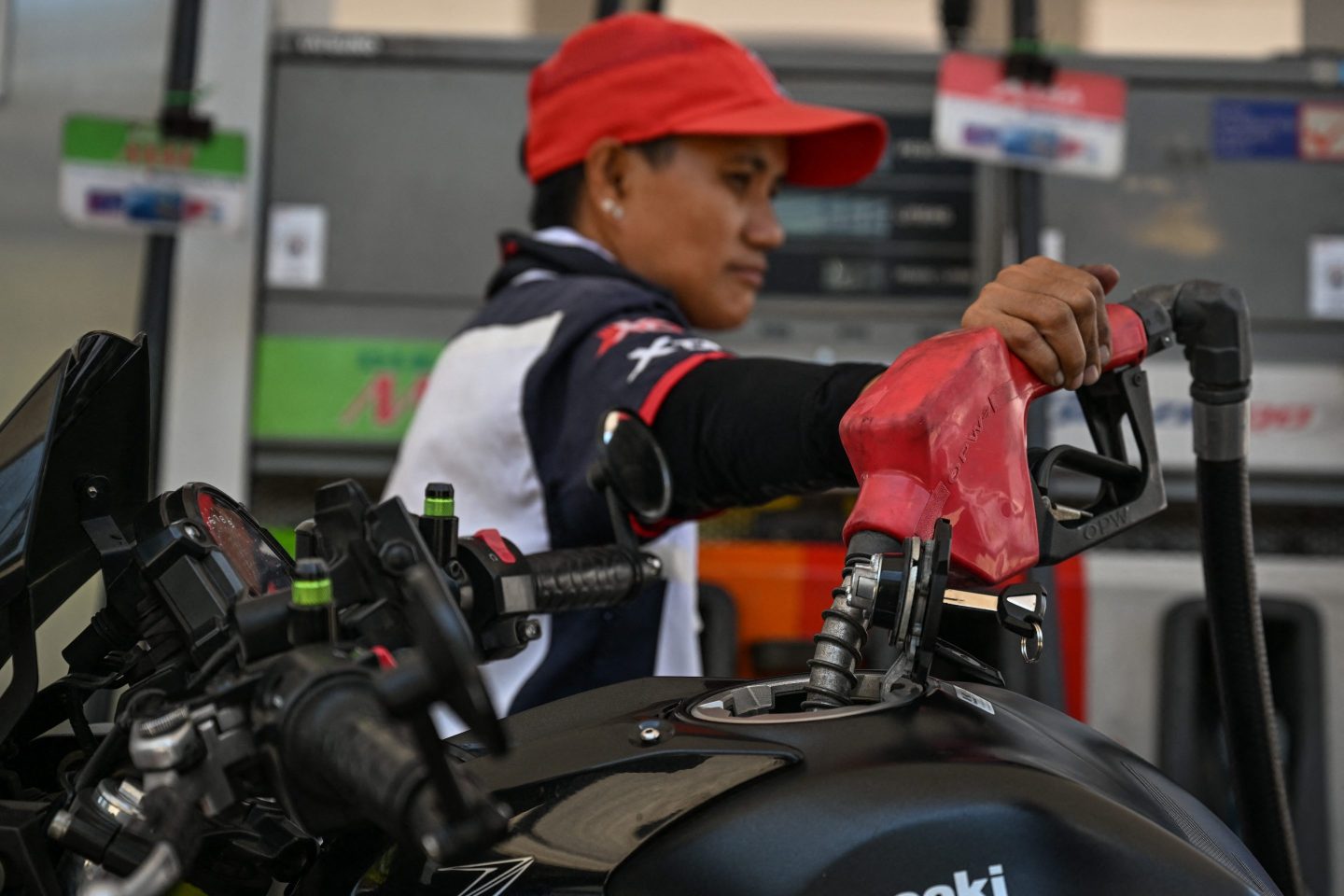 A person wearing a red hat has their hand on a gas pump.
