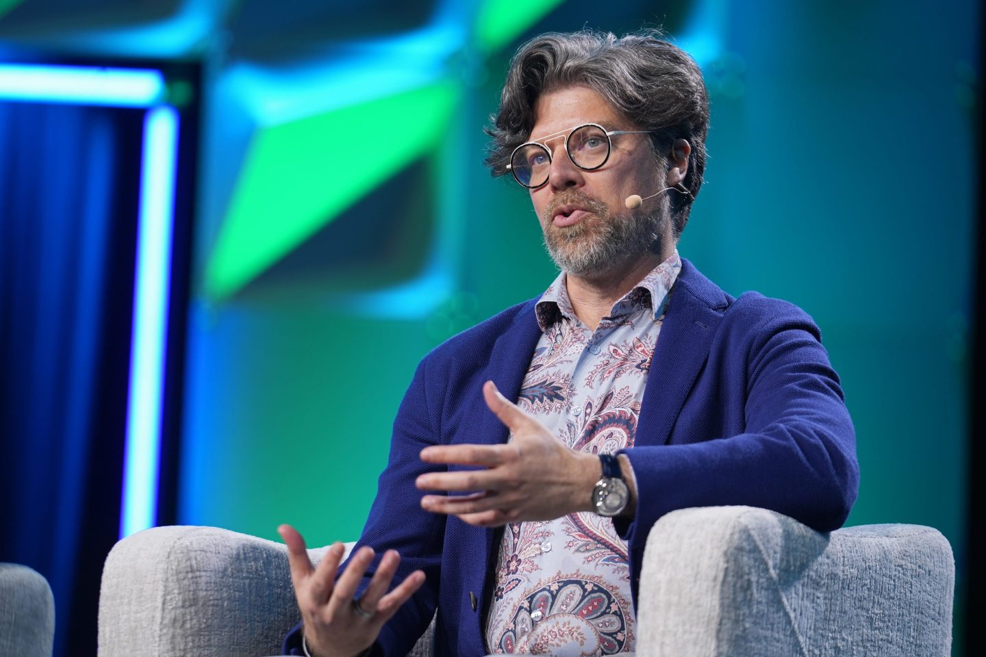 Bryan Catanzaro sits in a gray chair in front of a blue and green background.
