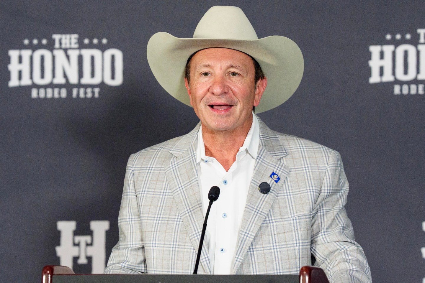 Landry speaks a podium wearing a white cowboy hat.