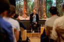 Sequoia partner Julien Bek sitting on a stool and holding a microphone while speaking to an audience. Behind him is a stage that looks like a forest.