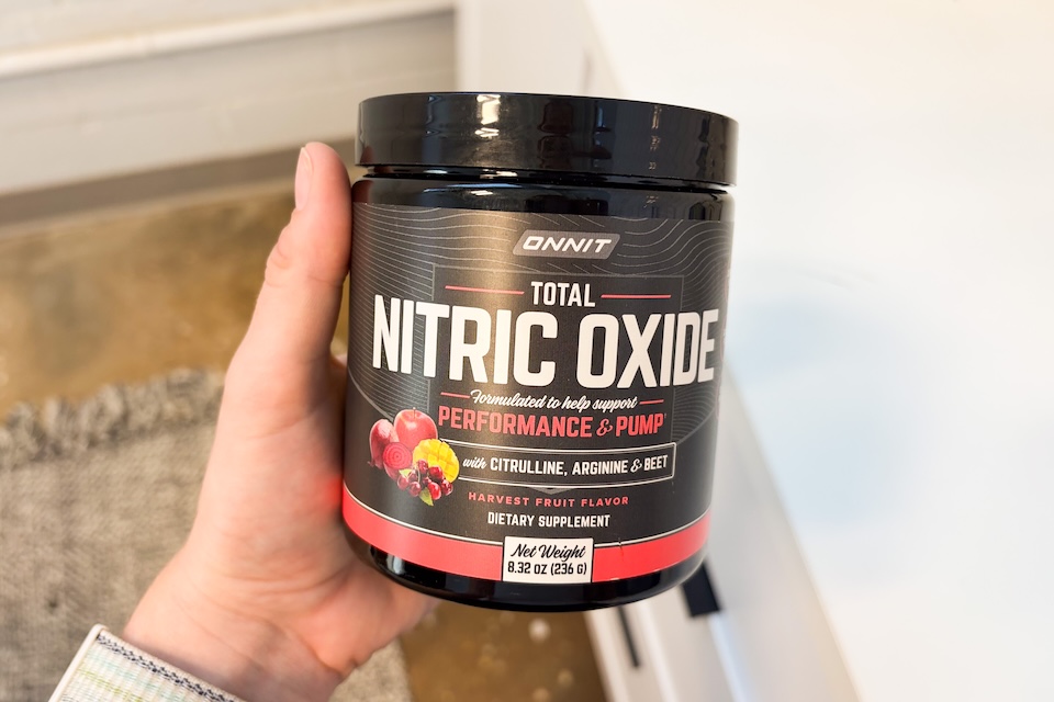 A hand holding a canister of Onnit Total Nitric Oxide.