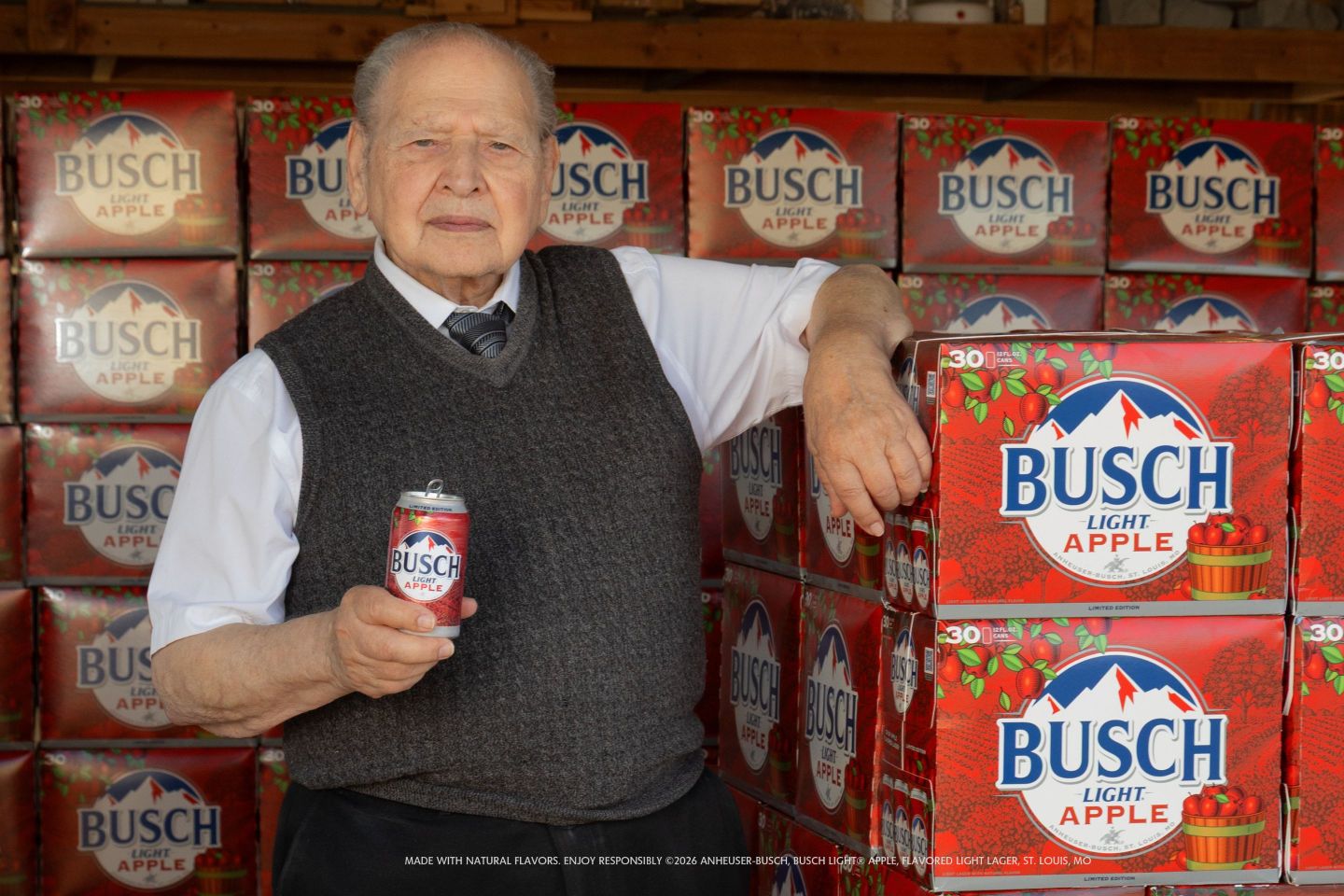 Ronald Wayne holding a can of Busch Light Apple, leaning up against a stacked package of the beer.