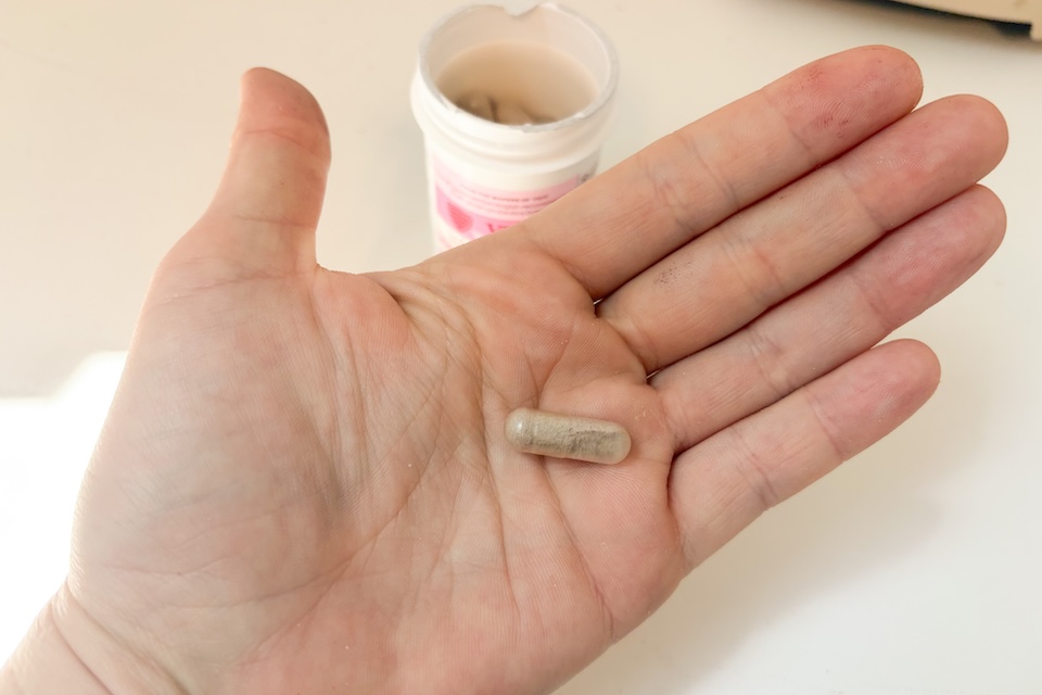 An open palm holding a VSL4 Vaginal Health probiotic capsule. You can see the bottle of probiotics in the background.