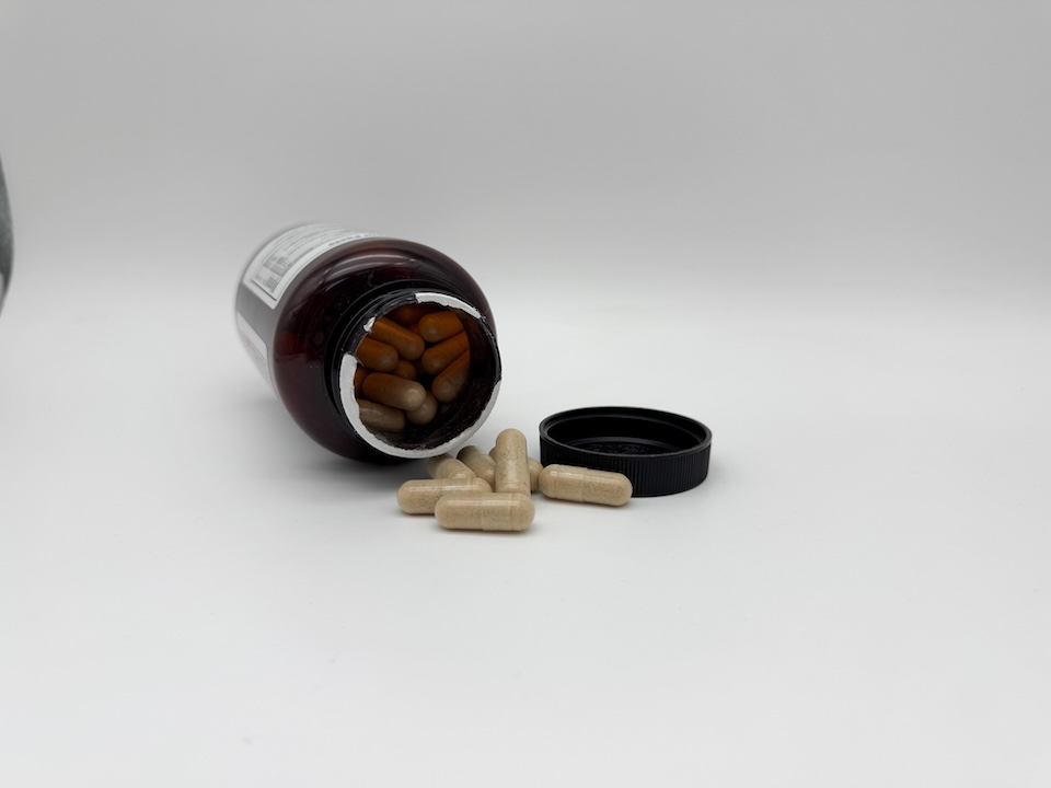 A bottle of Innerbody Labs Sleep Support lying on its side with some of the capsules spilling out. They are a tan color.