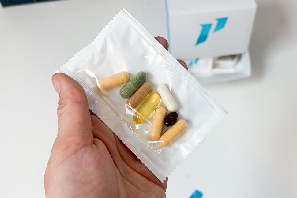 A hand holding a packet of 1st Phorm Micro Factor multivitamins. The packing is transparent, and you can see the multicolored supplements within.