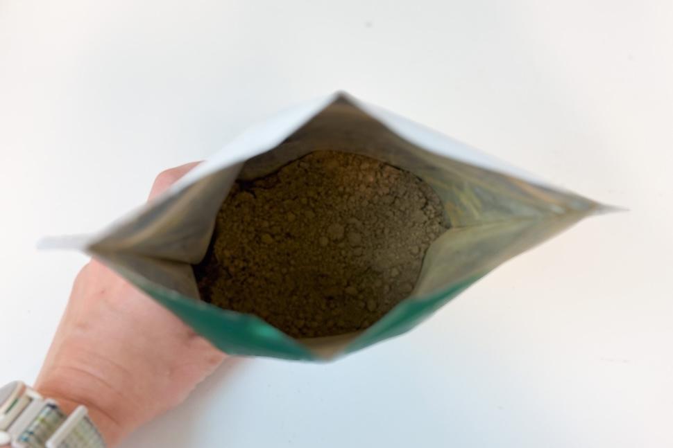 A hand opening a pouch of 1st Phorm Opti greens, showing the dark powder inside