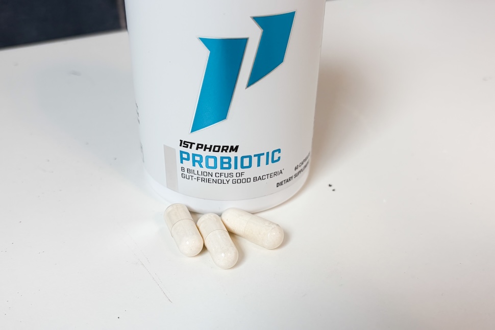 A bottle of 1st Phorm Probiotic sitting on a white countertop. Three off-white capsules have been placed next to it.