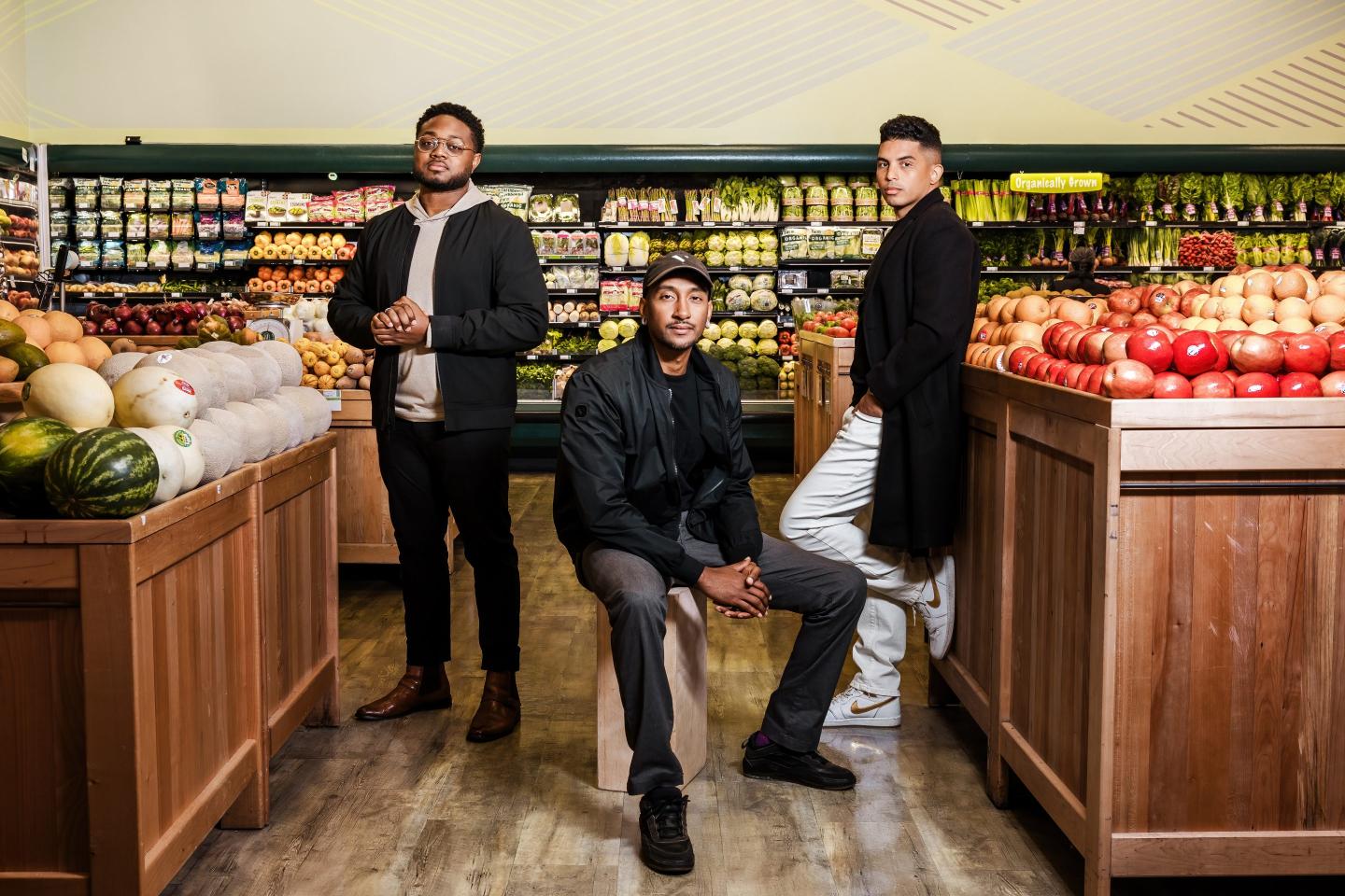 three men pose in a grocery store