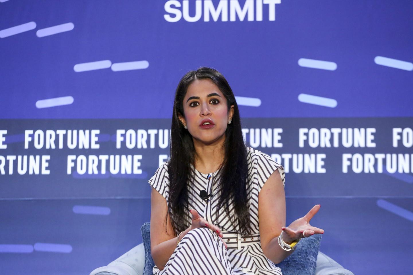 Hiba Mona Anver, wearing a black and white striped dress, gestures with her hands as she speaks onstage.